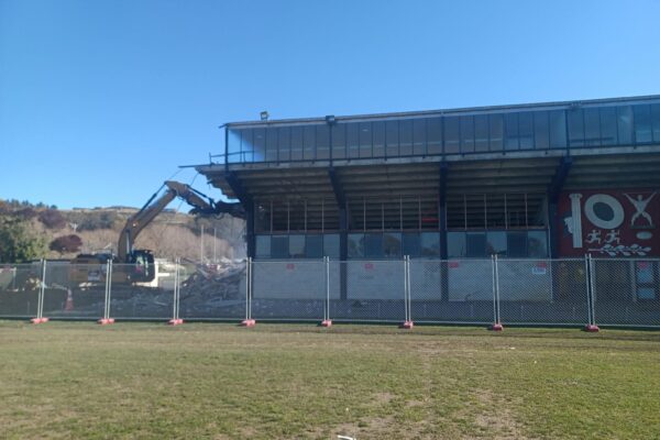 Image of excavator beginning the deconstruction and demolishment of North Otago rugby grandstand by Scope Group, NZ